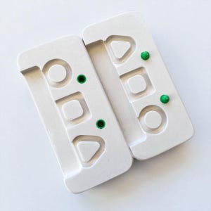 Peut inclure: Deux moules rectangulaires blancs avec des formes géométriques et des accents verts. Chaque moule a une forme de cercle, de carré et de triangle. Les moules sont faits d'un matériau solide et sont placés côte à côte.