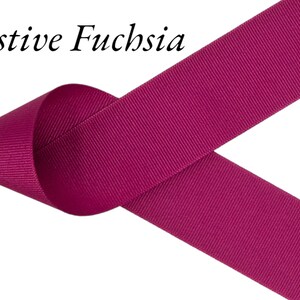Puede incluir: Primer plano de una cinta fucsia con el texto "Festive Fuchsia". La cinta est&aacute; doblada sobre s&iacute; misma, creando un bucle. La cinta tiene una textura acanalada y est&aacute; sobre un fondo blanco. El color de la cinta es rosa brillante.