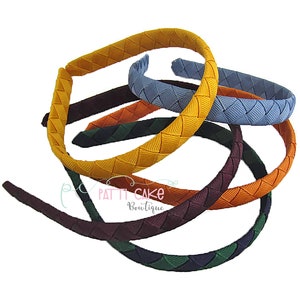 May include: A collection of colorful, braided headbands in various shades including yellow, blue, orange, and green. The headbands are made of a woven material and are displayed against a white background. The image includes the text "Patti Cake Boutique".