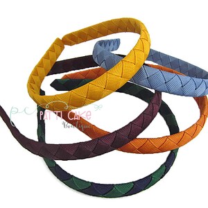 May include: A collection of colorful braided headbands in various shades, including yellow, blue, green, orange, and burgundy. The headbands are arranged in a circular pattern, showcasing their woven design. The image is set against a white background.