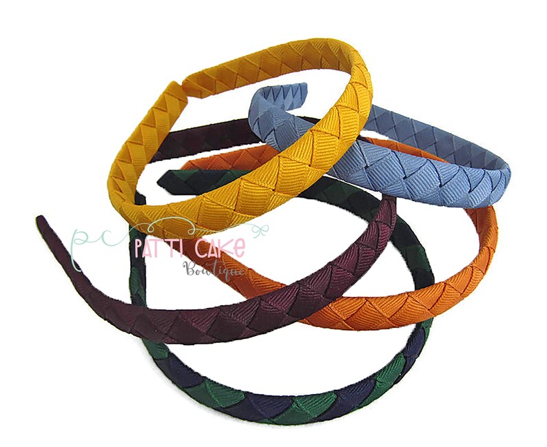 May include: A collection of colorful braided headbands in various shades, including yellow, blue, green, orange, and burgundy. The headbands are arranged in a circular pattern, showcasing their woven design. The image is set against a white background.