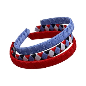 May include: Three woven headbands in red, light blue, and a red, white, and black pattern. The headbands are stacked, showcasing their braided texture and vibrant colors. The headbands are a stylish hair accessory.