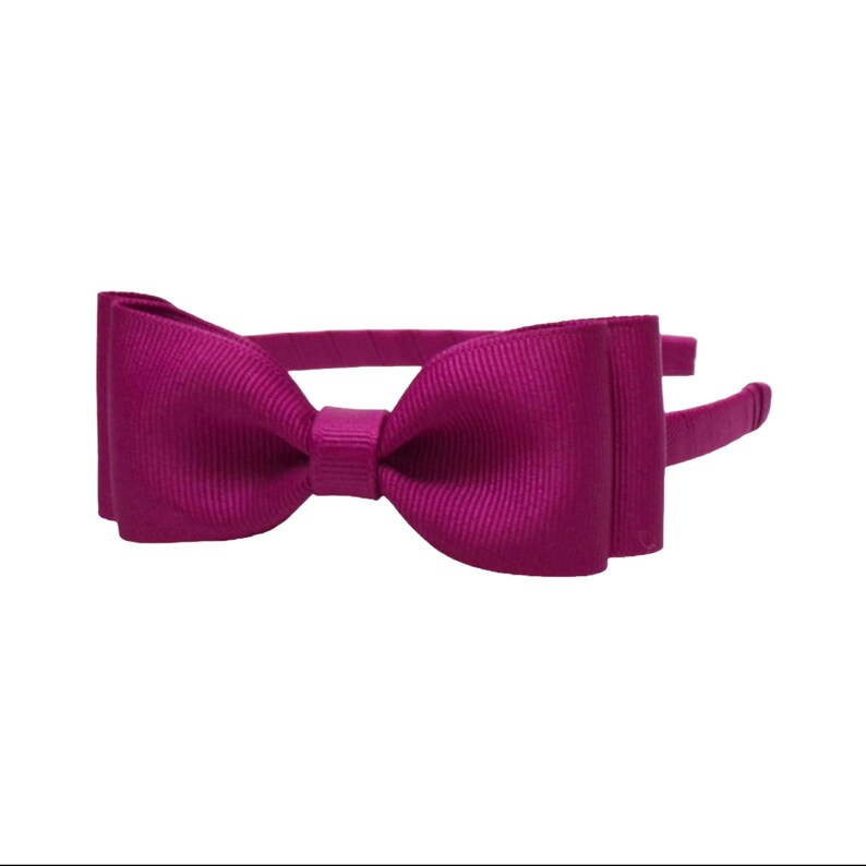 Puede incluir: Una diadema de color magenta con un lazo grande. El lazo est&aacute; hecho de una tela acanalada y est&aacute; centrado en la diadema. La diadema es de color liso y est&aacute; dise&ntilde;ada para ser usada en la cabeza.