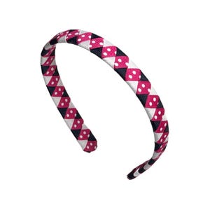 May include: A braided headband with a repeating pattern of pink diamonds with white polka dots, black diamonds, and white diamonds. The headband is curved and appears to be made of fabric.