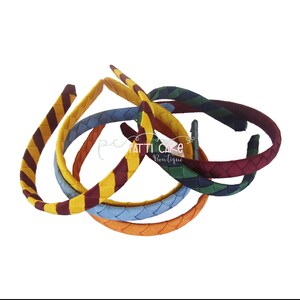 May include: A collection of braided headbands in various colors, including yellow with burgundy stripes, blue, orange, and green. The headbands are arranged in a loose pile, with the text "pc PATTI CAKE Boutique" visible.