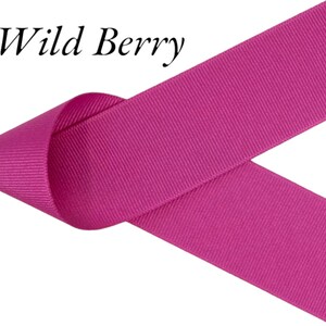Puede incluir: Primer plano de una cinta magenta vibrante con el texto "Wild Berry" en cursiva negra. La cinta est&aacute; doblada sobre s&iacute; misma, mostrando su textura y color sobre un fondo blanco. La cinta parece estar hecha de un material resistente.
