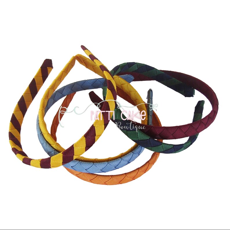 May include: A collection of braided headbands in various colors, including yellow, burgundy, blue, orange, and green. The headbands are arranged in a slightly overlapping pattern, showcasing their woven texture and design.