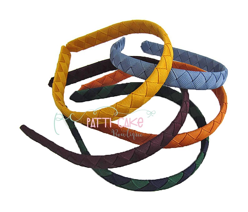 May include: A collection of colorful woven headbands in various shades, including yellow, blue, orange, and green. The headbands are arranged in a layered display, showcasing their braided texture. The image includes the text "Patti Cake Boutique".