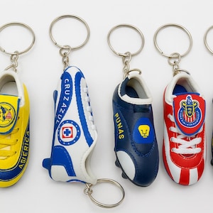 May include: Five soccer shoe keychains in yellow, blue, and red. Each keychain features a miniature soccer cleat with team logos and details. The keychains are attached to silver metal rings.
