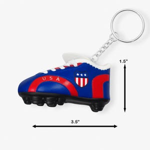 May include: A blue, red, and white soccer cleat keychain with the word "USA" and a shield emblem. The keychain is 3.5 inches long and 1.5 inches high. The keychain has a silver ring and chain.
