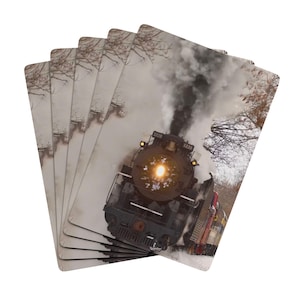 May include: Playing cards depicting a vintage steam train. The cards show a black locomotive with a bright headlight, emitting smoke, set against a snowy backdrop. The train is marked with the number "1225".