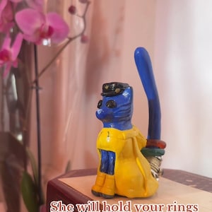 May include: A blue cat figurine wearing a yellow coat and a black hat, holding a blue wand. The image includes the text: "She will hold your rings and keep them safe <3."