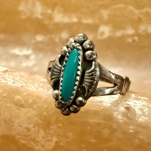 May include: Vintage silver ring with a turquoise stone. The ring features an oval turquoise stone set in a decorative silver setting with beaded and engraved details. The ring's design is reminiscent of Native American jewelry.
