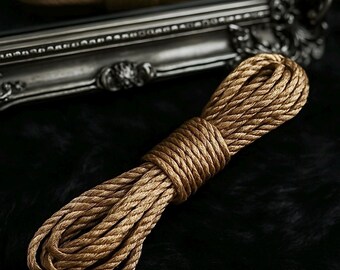 May include: A thick, brown rope coiled on a black surface. The rope is made of natural fibers and has a rustic look.