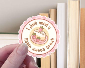 Può includere: Un adesivo rotondo smerlato con un bordo rosa chiaro e un centro color crema. L'adesivo presenta un disegno di una fetta di torta alle fragole su un piattino e il testo marrone "I just need a little sweet treat" scritto in cerchio.