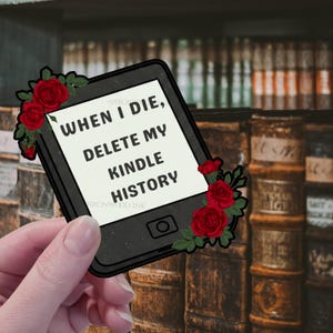 May include: A black e-reader shaped sticker featuring the text "WHEN I DIE, DELETE MY KINDLE HISTORY" in black capital letters on a white background, decorated with red roses and green leaves on the top left and bottom right corners.