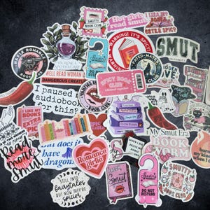 Pu&ograve; includere: Una collezione di adesivi in vinile assortiti con illustrazioni a tema librario, tra cui pile di libri, boccette di pozioni, peperoncini e cuori, con varie frasi come "Spicy Book Club", "Smut University" e "I paused my audiobook for this?"