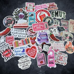 Pu&ograve; includere: Una collezione di adesivi in vinile assortiti con varie illustrazioni a tema librario, tra cui cuori, peperoncini, libri e testo come "Smut University", "Spicy Book Club", "Read more Smut" e "I paused my audiobook for this?"