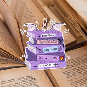 May include: A sticker featuring a stack of five purple books with a sword on top and wings on the sides. The book spines are labeled Fated Mates, Mystical Creatures, Chosen One, Slow Burn, and Fantasy, with small icons including a dragon and a heart.