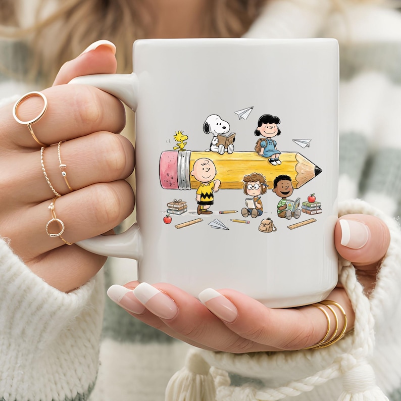 May include: White ceramic mug featuring a colorful illustration of Peanuts characters on a giant pencil. The design includes Snoopy, Charlie Brown, Lucy, and others, with books and paper airplanes. A fun, whimsical design for fans of the comic strip.