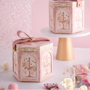 May include: Pink hexagonal gift boxes with carousel horse illustrations. The boxes have a ribbon handle and the text "Best wishes" and "Thank you". The boxes are decorated with carousel horses and the text "Happiness is a journey".