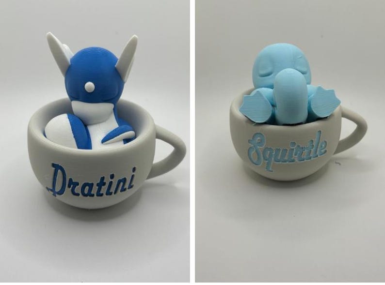 May include: Two ceramic teacups, each with a different Pok&eacute;mon figure inside. One cup has a blue and white Dratini, the other a light blue Squirtle. The names of the Pok&eacute;mon are written on the cups in blue.