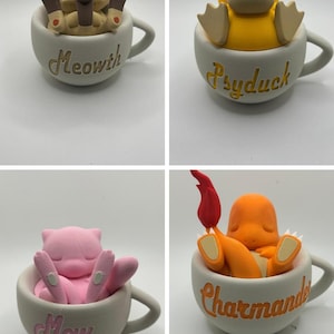 May include: Four ceramic teacups each feature a different Pokemon character: Meowth, Psyduck, Mew, and Charmander. Each character is resting inside the cup. The cups are white with the character's name in gold script.
