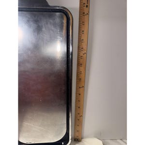 May include: A rectangular silver-toned metal tray with a dark border, positioned next to a wooden ruler. The ruler indicates the tray has a length of approximately 19 inches. The surface of the tray is reflective and shows signs of light wear.