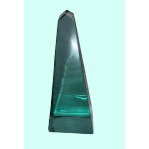 May include: A tall, emerald green glass obelisk with a faceted top. The triangular shape tapers upwards from a rectangular base. The transparent glass allows light to pass through, creating a shimmering effect. This decorative piece is suitable for home decor.