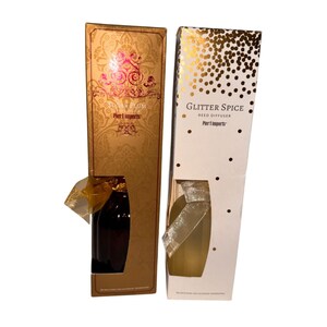 Puede incluir: Dos difusores de caña en cajas decorativas. Una caja es dorada con el texto "Sugar Plum" y la otra es blanca con purpurina dorada y el texto "Glitter Spice". Ambas cajas tienen una botella transparente.