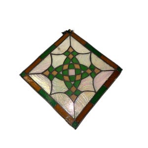 May include: A diamond-shaped stained glass panel featuring a central geometric knot pattern in green and tan. The design is surrounded by iridescent white glass segments and a dark brown border, all held together by thin dark metal lead lines.