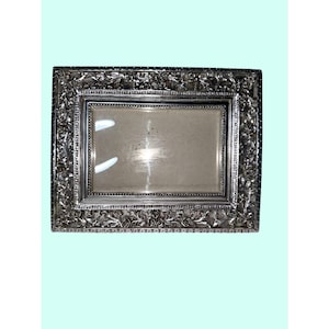May include: A rectangular silver picture frame with an ornate floral design. The frame has a clear glass insert and a detailed border with embossed flowers and leaves. The frame is likely made of metal and has a vintage or antique aesthetic.