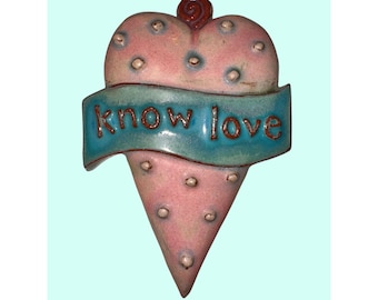 Könnte beinhalten: Rosa und blaue herzförmige Keramikdekoration mit den Worten "know love" auf einem blauen Banner. Das Herz hat eine strukturierte Oberfläche mit kleinen, erhabenen Punkten und einer Spirale oben. Die Dekoration hat die Form eines Eis.