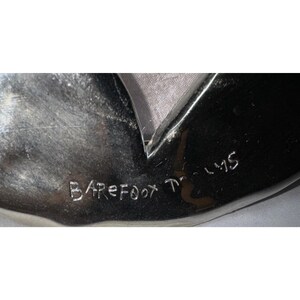 May include: A shiny, silver-colored object with a dark, reflective surface. The text "Barefoot Films" is etched into the surface. The object has a unique shape with a pointed edge.