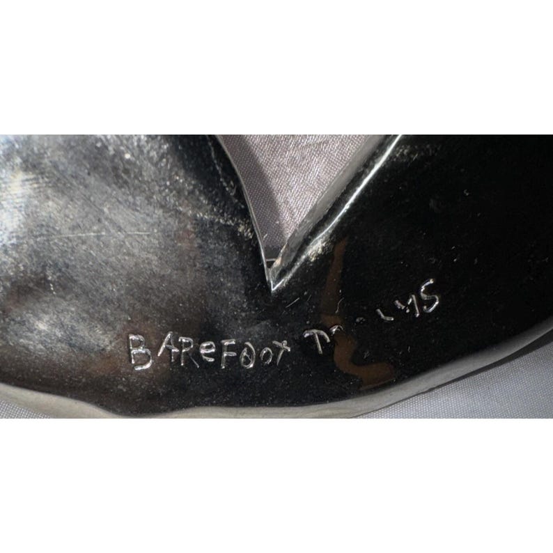May include: A shiny, silver-colored object with a dark, reflective surface. The text "Barefoot Films" is etched into the surface. The object has a unique shape with a pointed edge.
