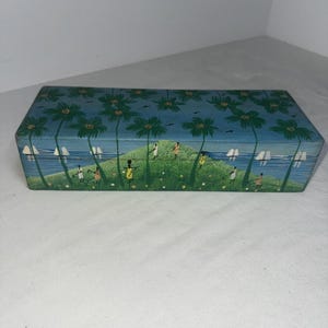 May include: A rectangular wooden box with a painted scene of palm trees, a beach, and people. The box is painted in shades of blue, green, yellow, and white.