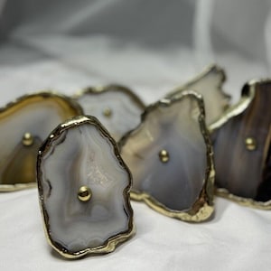 May include: Five agate drawer pulls with gold trim and a gold knob in the center of each. The agate is in shades of brown, gray, and white.