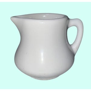 以下が含まれることがあります： 曲線的なボディとハンドルが付いた、小さな白いセラミックピッチャー。ピッチャーには注ぎやすい注ぎ口が付いています。背景は水色です。