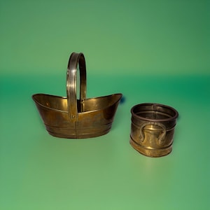Puede incluir: Dos recipientes de latón, uno con asa y el otro de forma redondeada. Ambos están hechos de un metal brillante de color dorado.