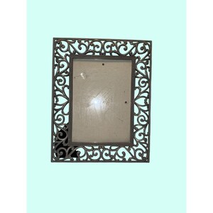 May include: A rectangular picture frame with a dark bronze finish and an intricate, openwork scrollwork border. The inner edge of the frame features a beaded texture surrounding a clear glass pane with visible surface smudges and marks.