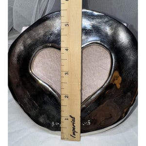 May include: A silver-colored heart-shaped picture frame with a light pink interior. The frame is approximately 5 inches tall, as measured by a wooden ruler. The frame has a unique, irregular shape.