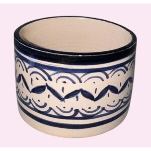 Pode incluir: Um recipiente cilíndrico de cerâmica com interior e exterior creme. O exterior é decorado com um padrão repetitivo de linhas curvas azuis e formas semelhantes a folhas, com uma faixa azul escura na parte superior e inferior.