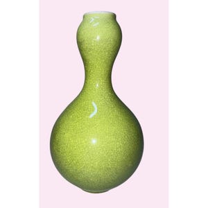 Puede incluir: Un jarrón de cerámica verde con una forma de calabaza única. El jarrón tiene una superficie texturizada y agrietada y un cuello estrecho. El jarrón es de un color verde brillante y primaveral y tiene un acabado brillante. Este jarrón decorativo es adecuado para la decoración del hogar.
