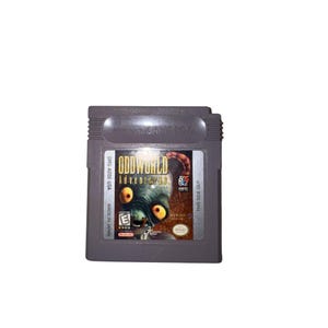 May include: A gray Nintendo Game Boy video game cartridge for Oddworld Adventures. The label features a large-eyed creature, the title text, an E rating symbol, and the text DMG-AODE-USA, Made in Japan, and This Side Out printed on the front.