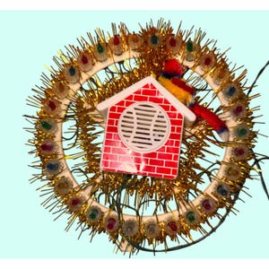 May include: Vintage Christmas tree topper with a red and white birdhouse design. The birdhouse has a speaker and is surrounded by a white ring with colorful lights and gold tinsel. A red, yellow, and blue bird sits on top.