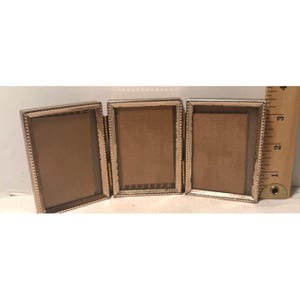 Op de afbeelding: Een zilverkleurige metalen triptiek fotolijst met drie rechthoekige openingen met kralenranden. Een houten liniaal is verticaal aan de rechterkant geplaatst en toont een framehoogte van ongeveer 8,9 cm.