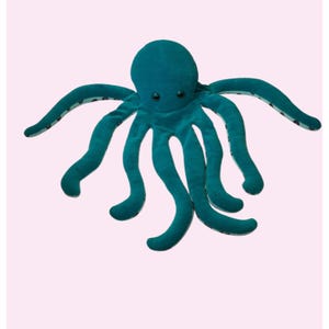 May include: A plush octopus toy in a deep teal color. The stuffed animal features a rounded head, eight long curved tentacles, and two small dark eyes. The underside of the tentacles shows a lighter teal fabric with a subtle dark pattern.