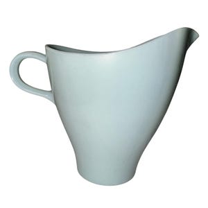 May include: A light blue pitcher with a curved handle and a spout. The pitcher has a unique, asymmetrical design, with a wide opening and a tapered base. The pitcher is made of a smooth, glossy material.