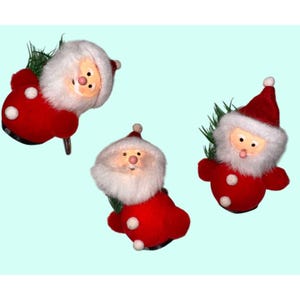 Pode incluir: Três enfeites de Natal em forma de Papai Noel. Cada Papai Noel tem um terno vermelho com bolinhas brancas, barba branca e chapéu vermelho. Os enfeites têm um fundo azul claro e são decorados com pequenos galhos verdes.