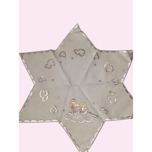 May include: A star-shaped, light gray decorative cloth with a scalloped edge. The cloth features embroidered clouds, stars, and two figures on a cloud. The edges are trimmed with a silver border.